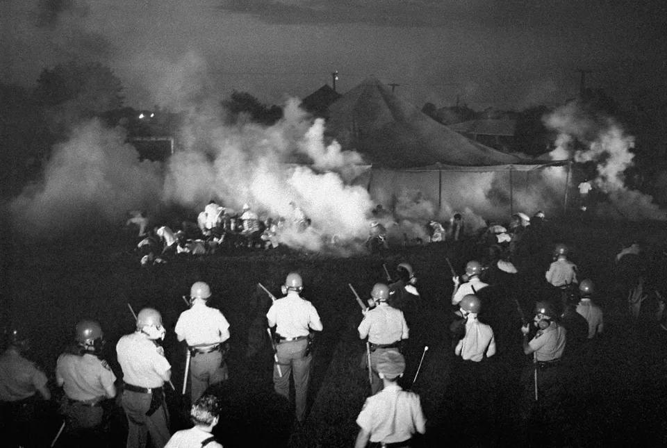 Police officers in gas masks move across a yard among tents
