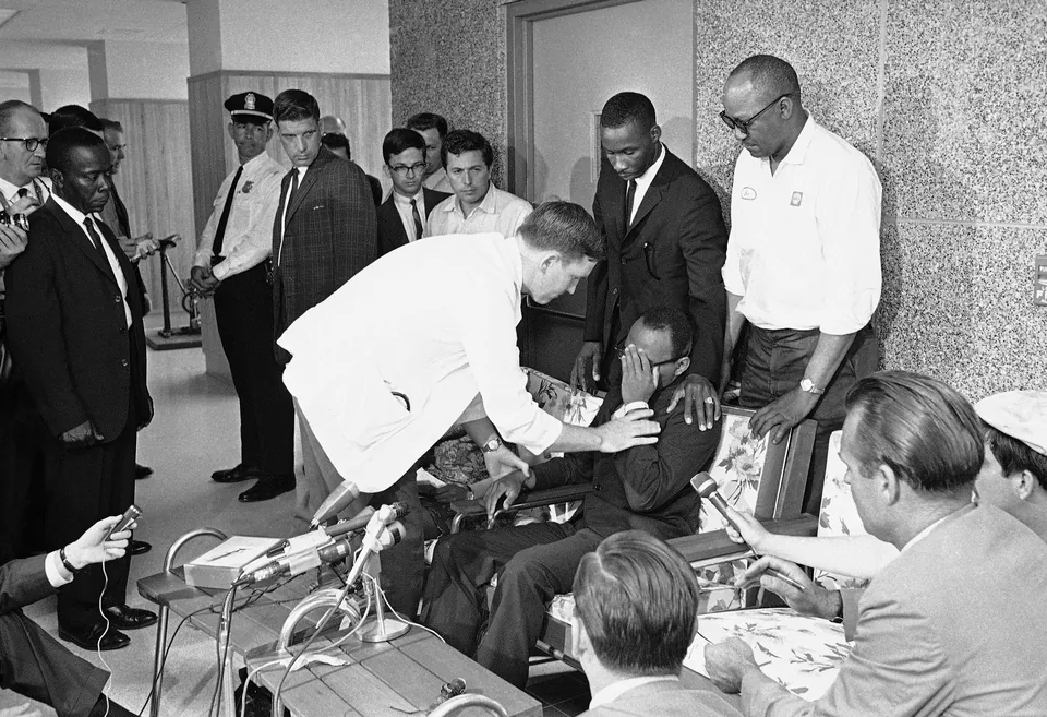 A doctor bends over James Meredith as he sits at a press conference