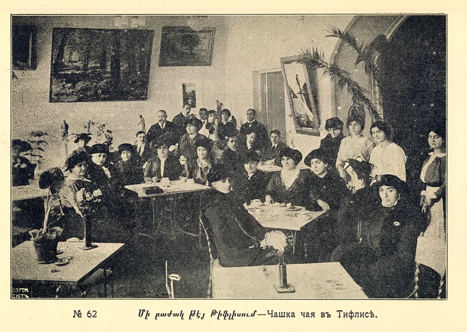 People sit and stand at tables during a tea gathering
