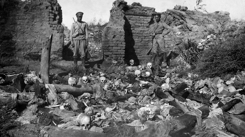 Servicemen stand behind human remains lying on open ground