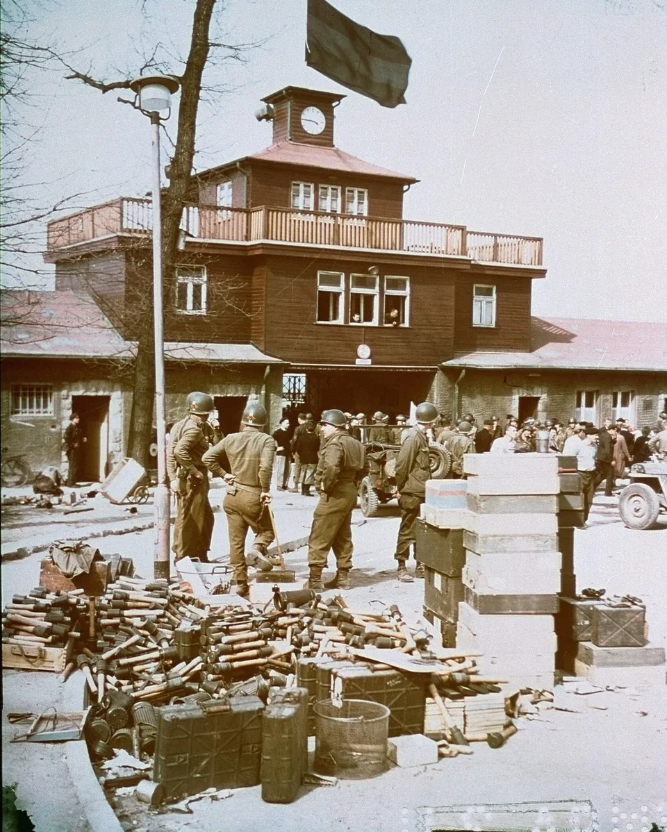 American soldiers stand outside the camp gate building and its clock tower, with crates and ammunition in front of them