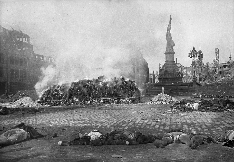 Ряд погибших на брусчатке, горящий костёр и памятник на дальнем плане.
