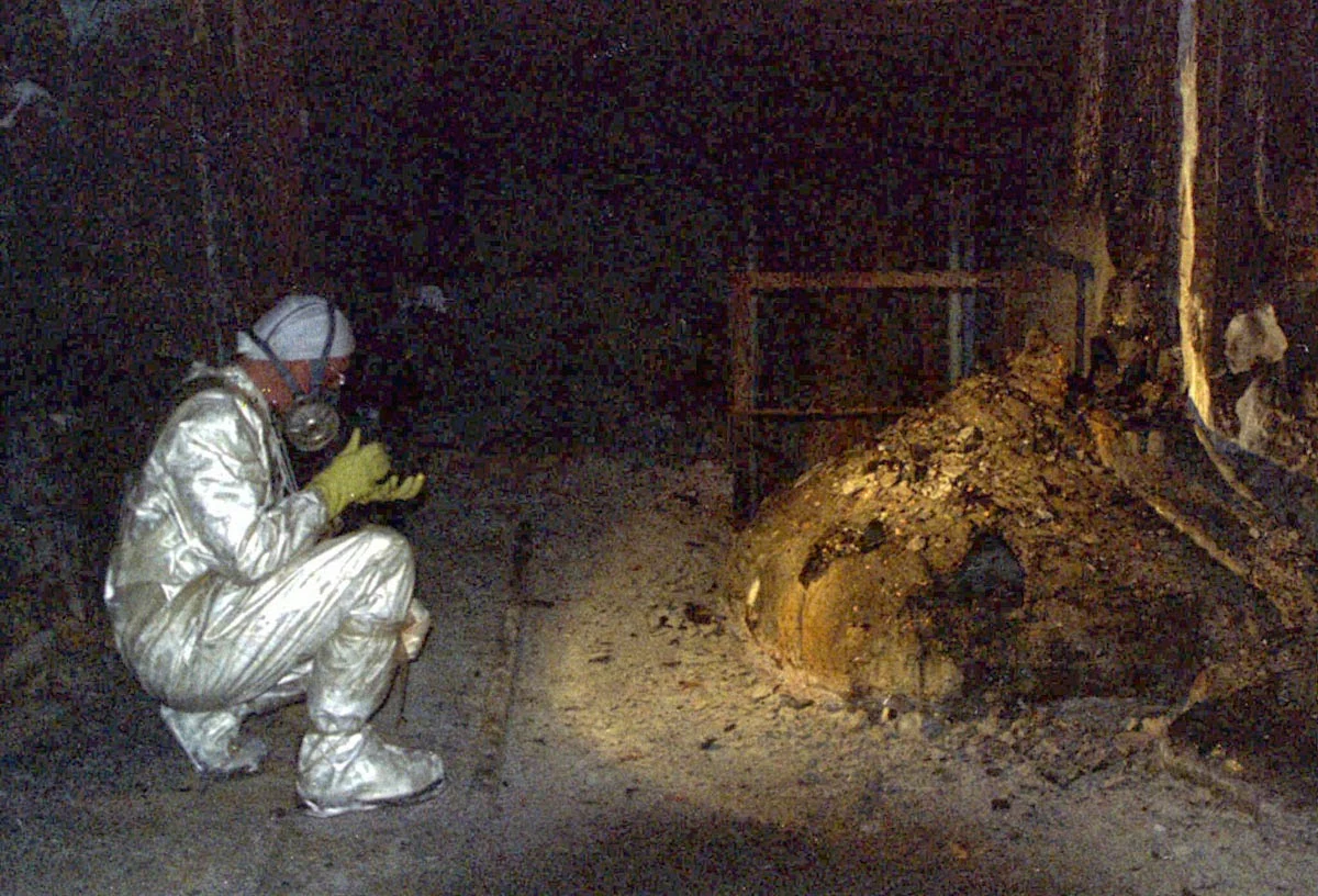A person wearing protective clothing and a respirator crouches beside the Elephant’s Foot. The photograph is held by Universal History Archive / Universal Images Group and published by Getty Images. The person, photographer and date have not been identified.