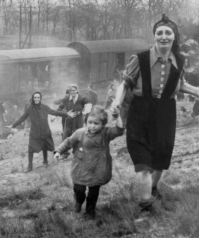 Женщина держит ребёнка за руку на склоне. Позади другие люди поднимаются от вагонов.
