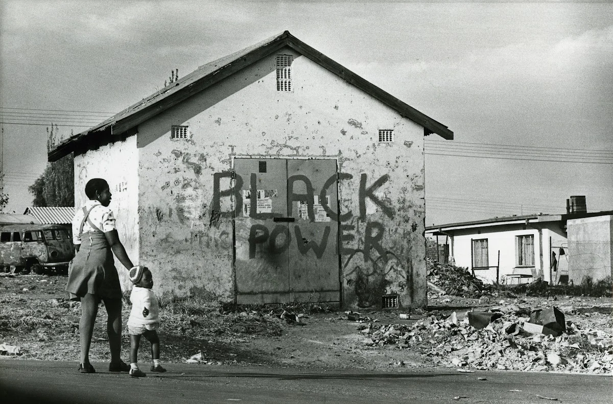 Женщина и ребёнок идут вдоль стены с крупной надписью «BLACK POWER».