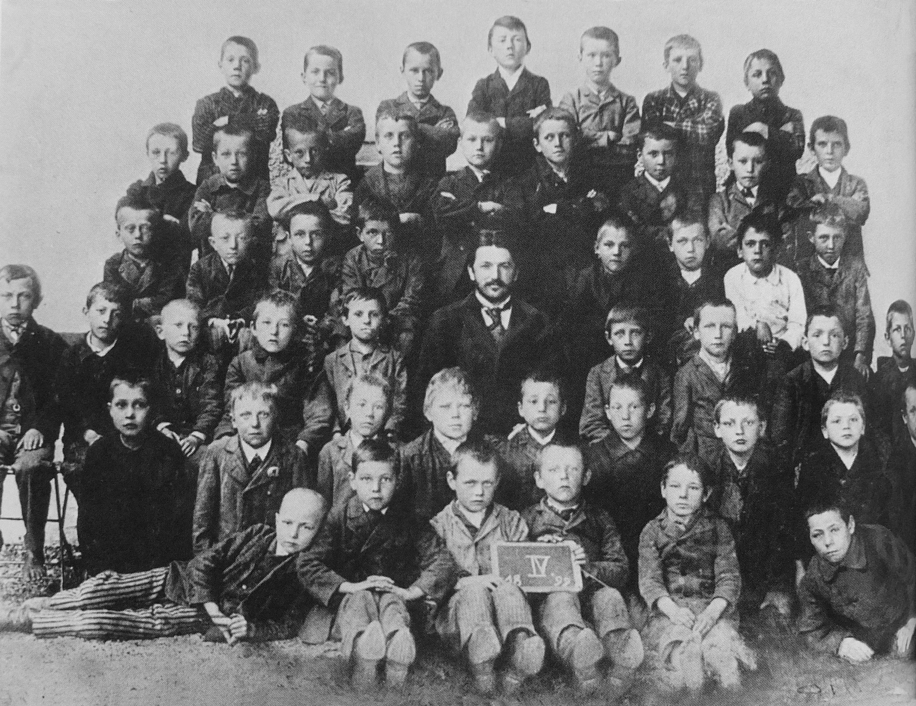Общий школьный снимок: ученики в нескольких рядах вокруг учителя; Гитлер стоит в верхнем ряду, ближе к середине.