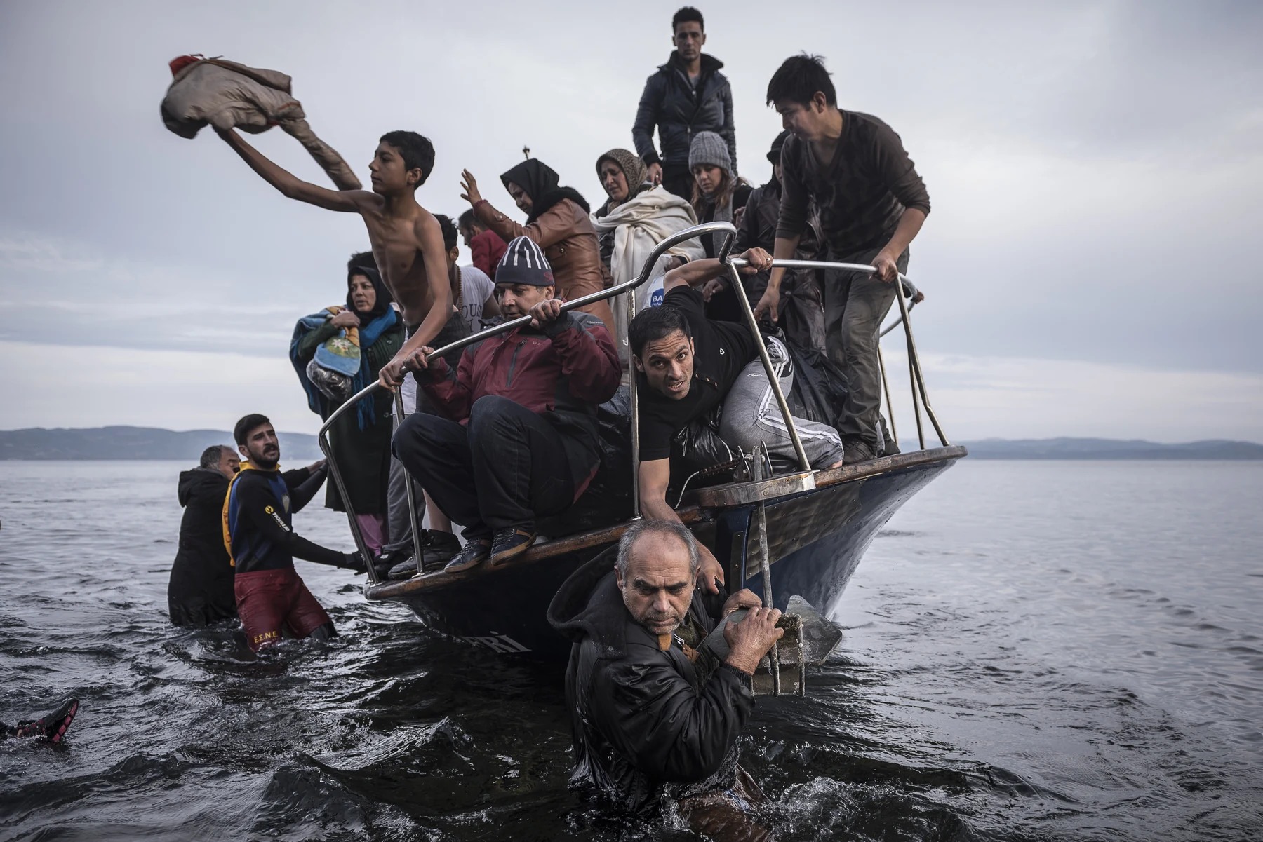 A crowded boat near shore; several men stand in the water beside it.