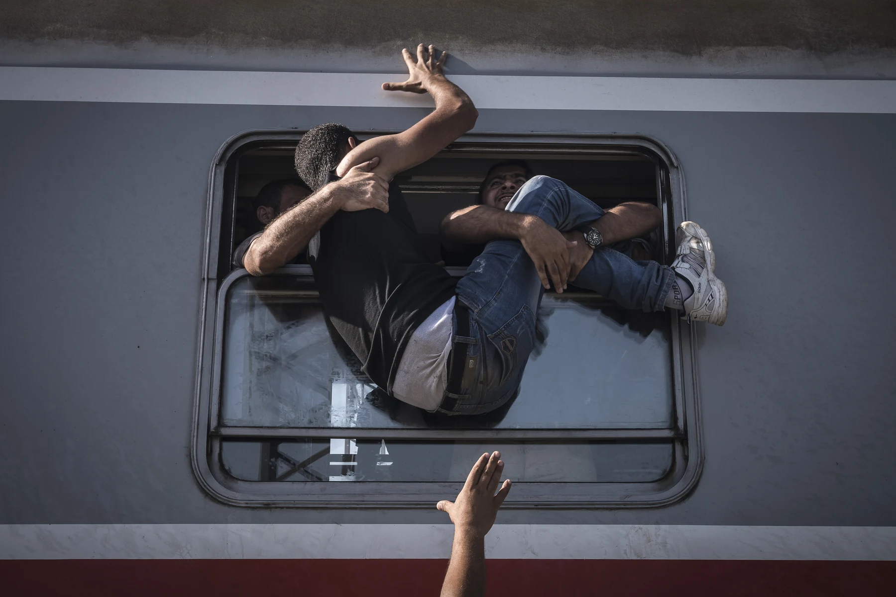 People inside the carriage help a man climb through an open window.