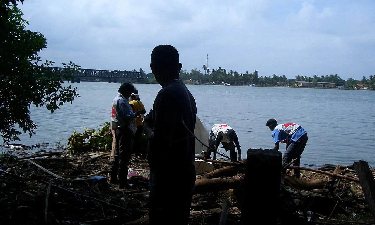 People and a boat on shore, with Kallady Bridge behind. Batticaloa, Sri Lanka; file metadata gives 28 December 2004.