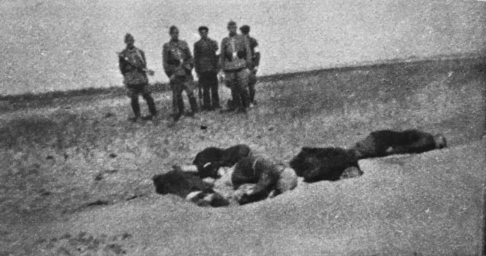 Five armed men, four in uniform and one in civilian clothes, stand behind bodies lying on the ground