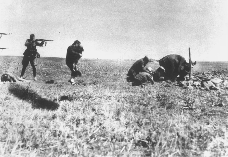 A uniformed man aims a rifle at a woman holding a child; other people bend towards the ground at right, with two more gun barrels visible at left
