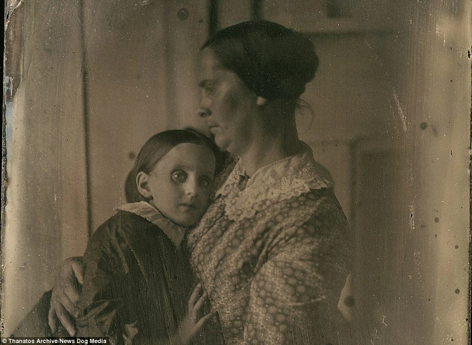 A woman sits beside a child facing the camera. The copy bears a Thanatos Archive / News Dog Media mark, but no open catalogue record establishes the names, date or circumstances.