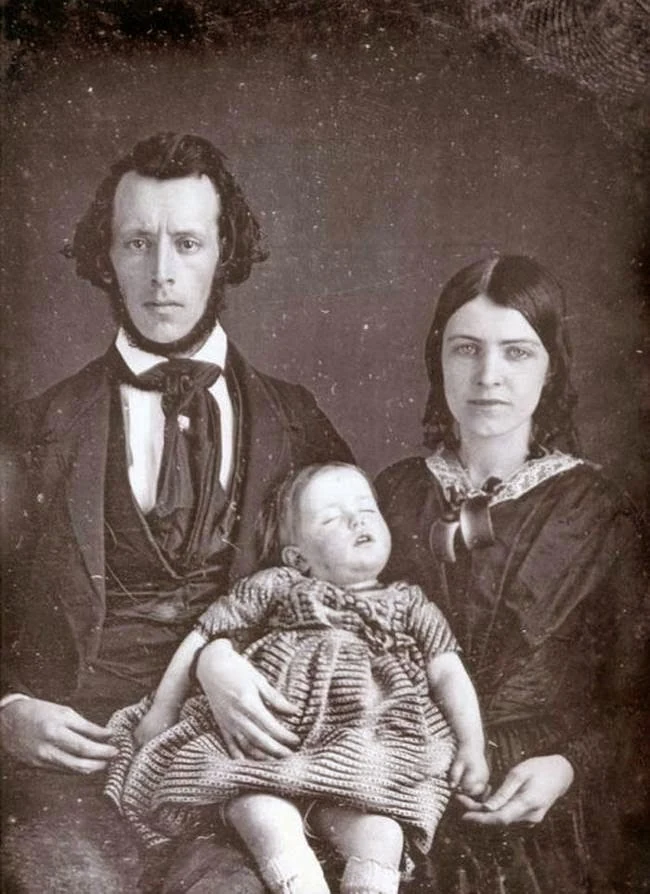 A man and woman sit before the camera; the woman holds a baby with closed eyes. Online posts say the baby was dead. No archival record confirms the sitters’ identities, relationship or a post-mortem sitting.