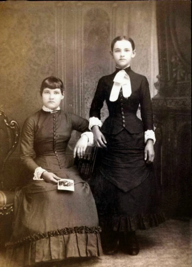 One woman sits and another stands. Online lists call the standing woman deceased because her hands appear dark. Their colour cannot establish a post-mortem photograph; no archival description has been found.