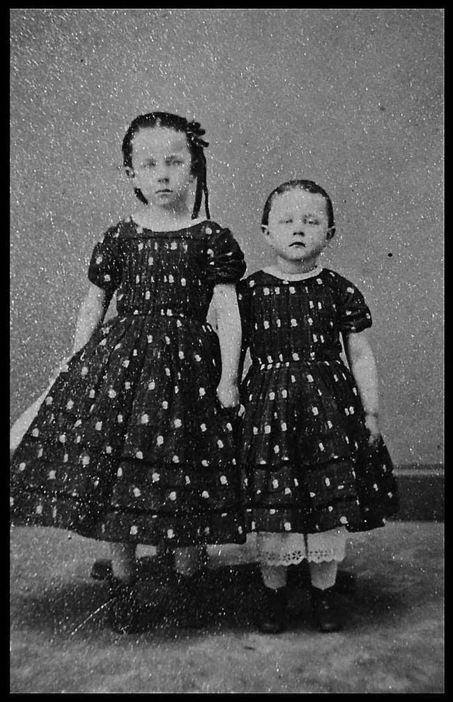 Two girls stand holding hands in matching dresses. The photograph is known from online post-mortem collections; the available copy has no names, date, card reverse or archival record.