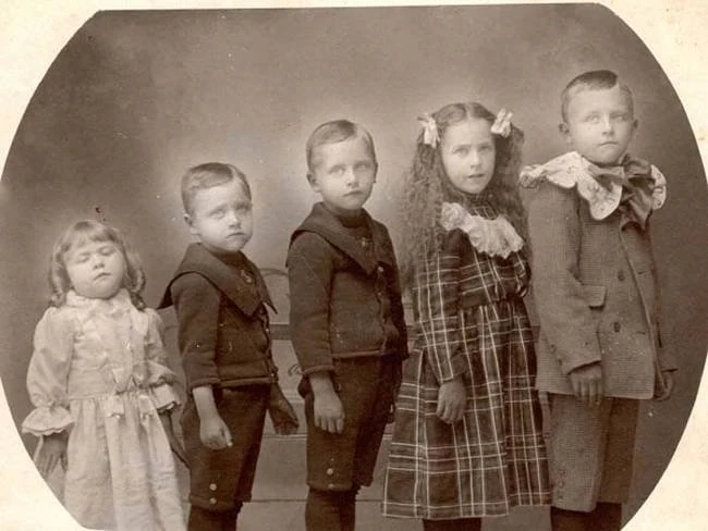 Five children face the camera; the girl on the left has her eyes closed. An online caption calls her deceased. Closed eyes cannot establish that, and no primary record identifies the children or the circumstances.