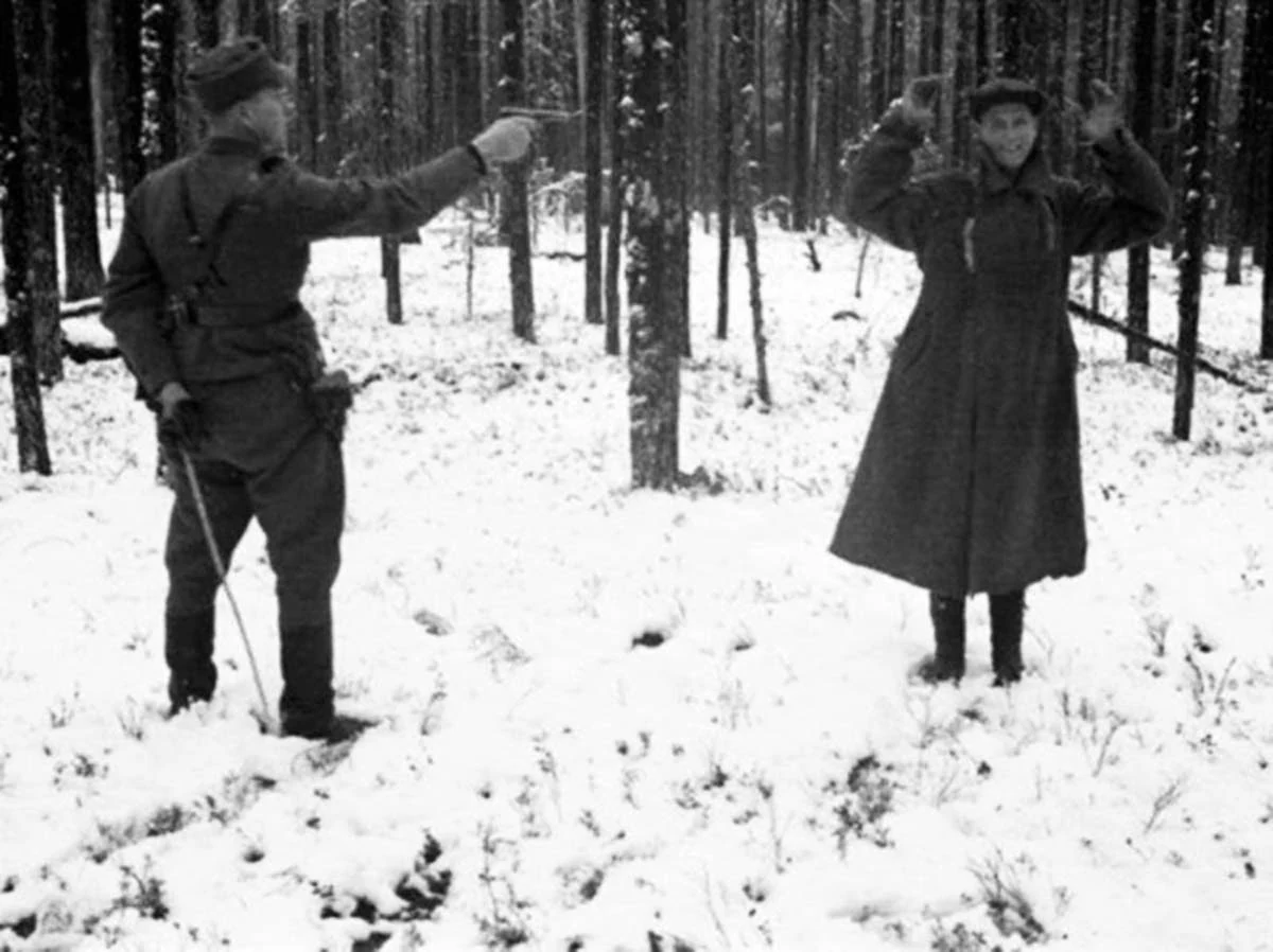 Человек с поднятыми руками стоит перед финским военнослужащим, направившим на него пистолет