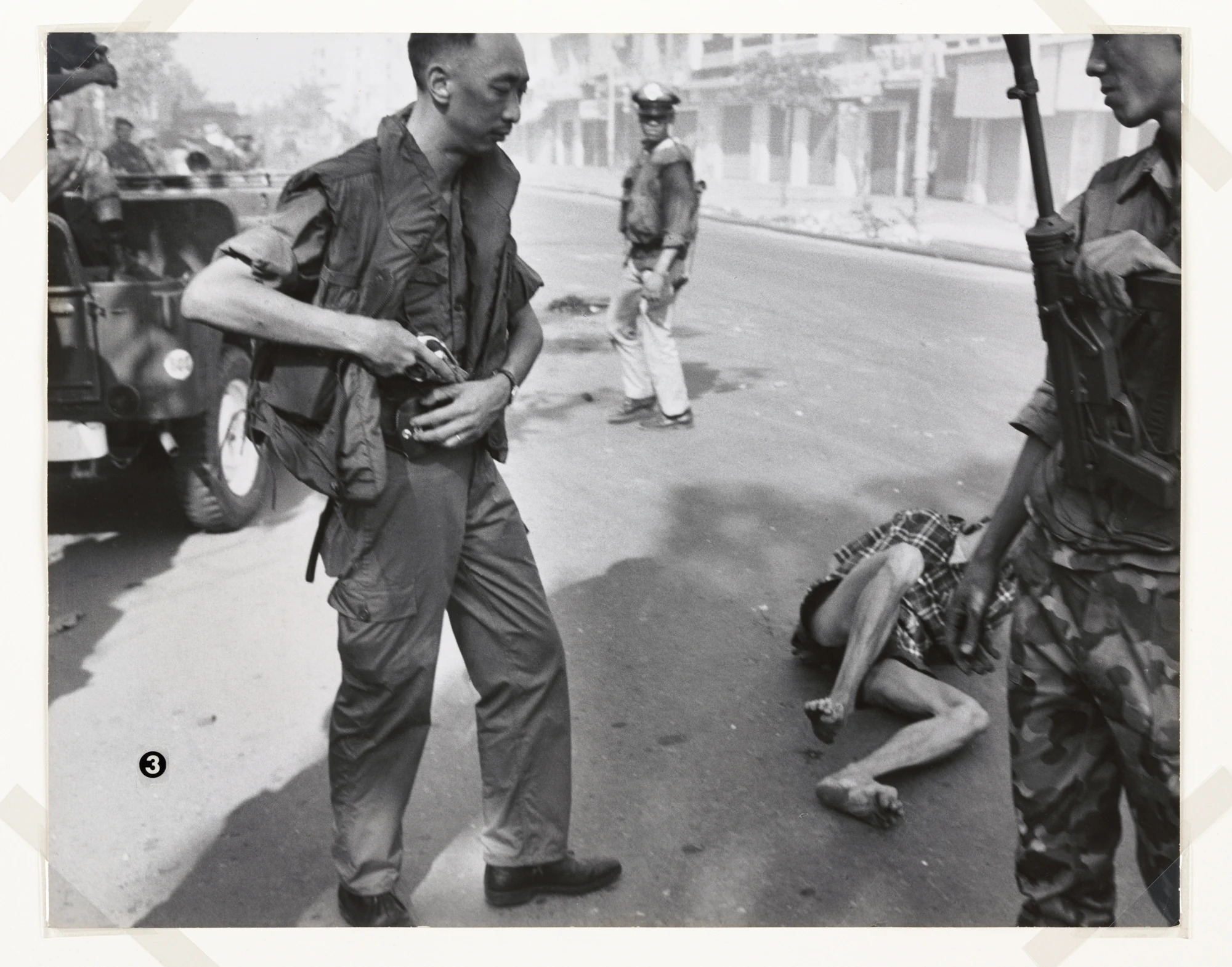Nguyễn Ngọc Loan stands at left with his revolver by his waist. At right, beyond a soldier in the foreground, lies Nguyễn Văn Lém’s body. Eddie Adams / Associated Press.