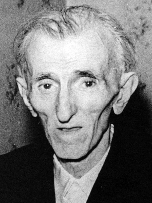 An elderly Nikola Tesla in a dark jacket and light shirt looks at the camera