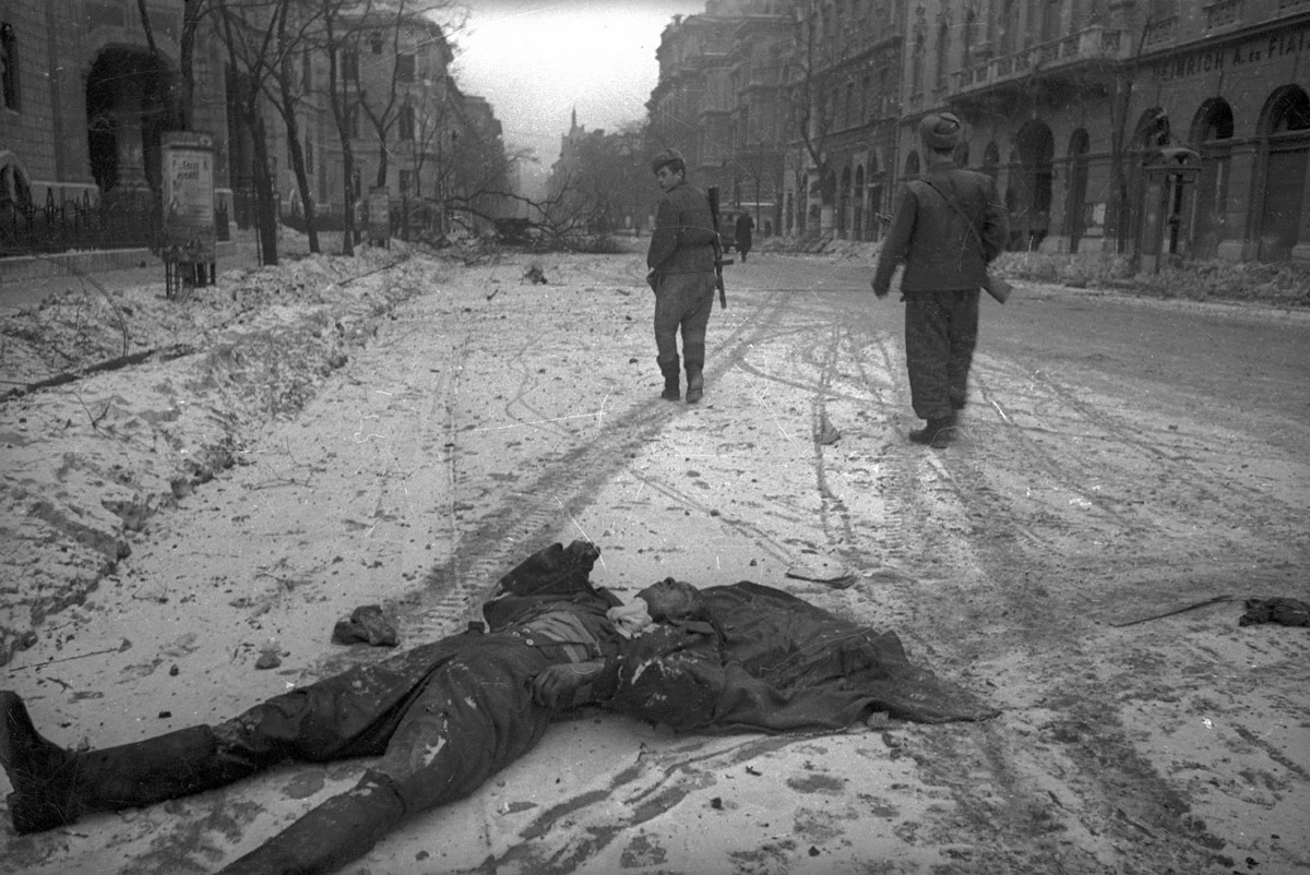 Тело лежит на заснеженной мостовой; по улице идут люди.